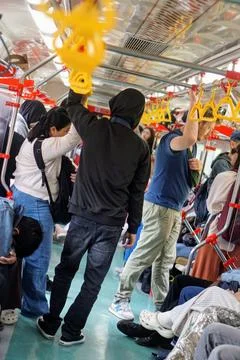 Passengers stand while holding yellow handrails in a crowded commuter electric Stock Photos