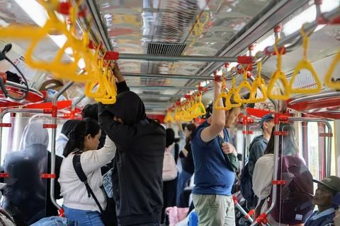 Passengers stand while holding yellow handrails in a crowded commuter electric Stock Photos