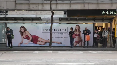 Passengers wait for a bus in front of a light box advertising of lingerie Stock Footage 45083102