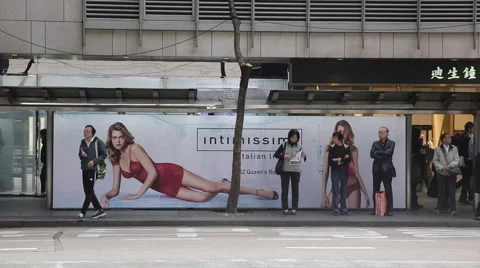 Passengers wait for a bus in front of a light box advertising of lingerie Stock Footage 45083196