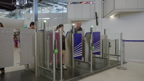 Passengers walk through automated turnstiles inside an airport terminal Stock Footage 336725892