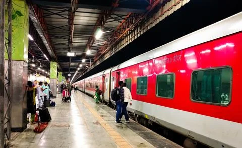 Passengers walking beside sleeper train at Indian railway station platform. Stock Photos