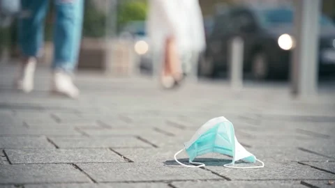 A passer-by steps on a used, discarded face mask lying on the sidewalk. Stock Footage 140105350