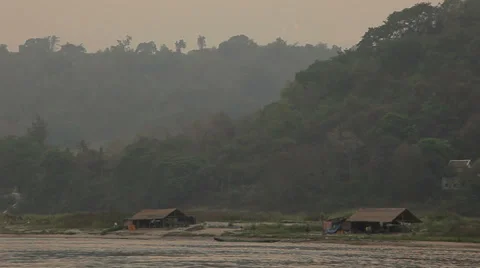 Passing huts on the Mekong River. Jungle hills in the background. Stock Footage 38037090