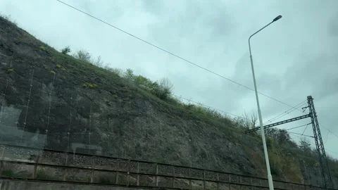 Passing railway track alongside steep rocky embankment, protective mesh covering Stock Footage 333163797