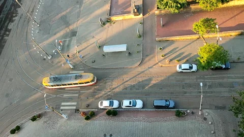 Passing tram road intersection Road tram people parked cars green trees shadows Stock Footage 327540188