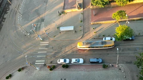 Passing tram road intersection Road tram people parked cars green trees shadows Stock Footage 327540191