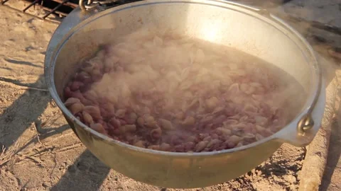 Pasta with beans is cooked in a metal cauldron on a bonfire in nature Video stock 134348212