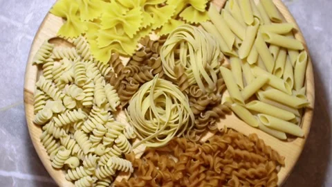 Pasta of different types on a round wooden plate rotates in a circle Stock Footage 220684839
