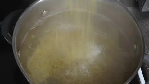 Pasta falling into boiling hot water in a saucepan, steam rises from the water Stock Footage 166338412