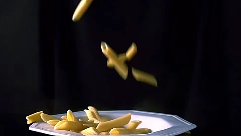 Pasta falling into a white plate on a black background Stock Footage 233372223