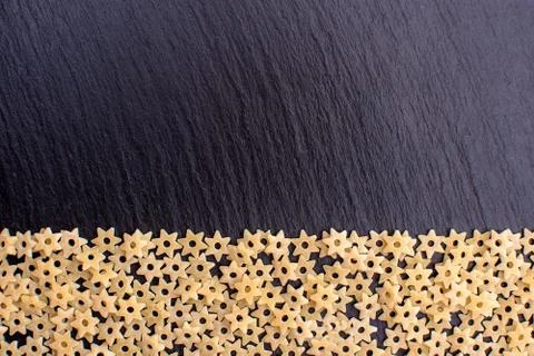Pasta in the form of asterisks rests on a black background of a stone board,  Stock Photos