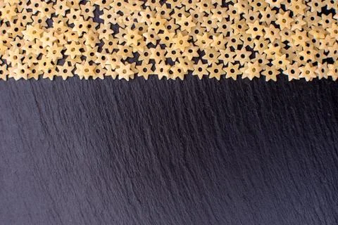 Pasta in the form of asterisks rests on a black background of a stone board,  Stock Photos