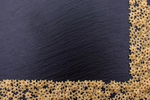 Pasta in the form of asterisks rests on a black background of a stone board,  Stock Photos