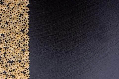 Pasta in the form of asterisks rests on a black background of a stone board,  Stock Photos