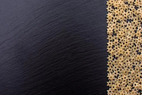 Pasta in the form of asterisks rests on a black background of a stone board,  Stock Photos