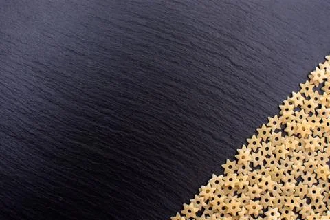 Pasta in the form of asterisks rests on a black background of a stone board,  Stock Photos