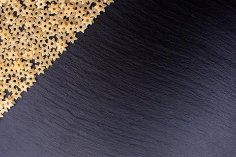 Pasta in the form of asterisks rests on a black background of a stone board,  Stock Photos