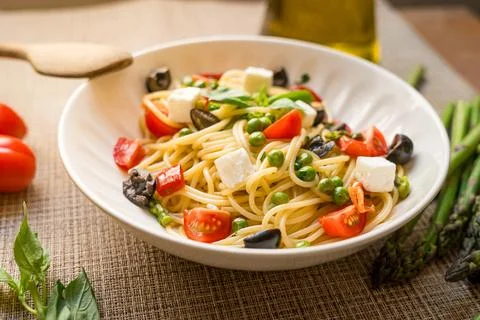 Pasta primavera spaghetti close up with cherry tomatoes, black olives, feta 库存照片