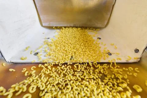 Pasta production process showcasing macaroni being formed and extruded in a Stock Photos
