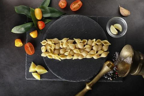 Pasta shells on black stone. Tomatoes and bay leaves with allspice and sea .. Stock Photos