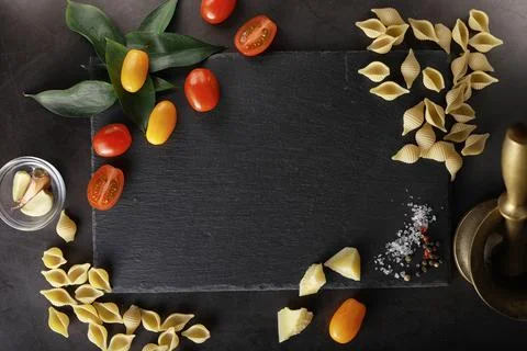 Pasta shells on black stone. Tomatoes and bay leaves with allspice and sea .. Stock Photos