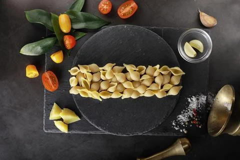 Pasta shells on black stone. Tomatoes and bay leaves with allspice and sea .. Stock Photos