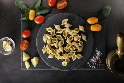 Pasta shells on black stone. Tomatoes and bay leaves with allspice and sea .. Stock Photos
