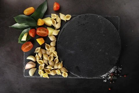 Pasta shells on black stone. Tomatoes and bay leaves with allspice and sea .. Stock Photos