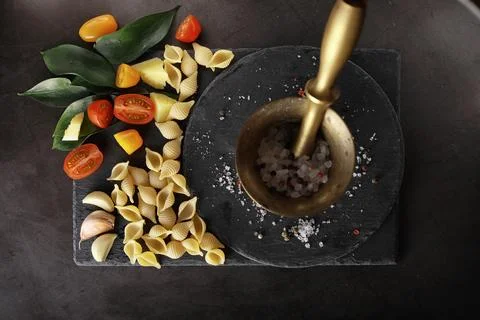 Pasta shells on black stone. Tomatoes and bay leaves with allspice and sea .. Stock Photos