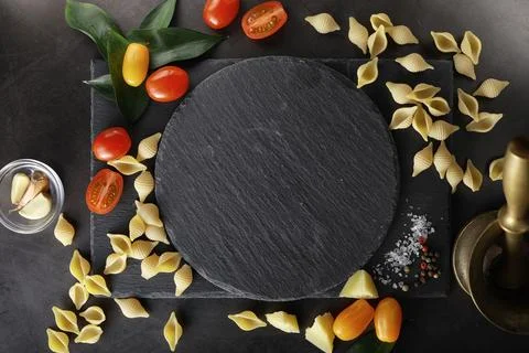 Pasta shells on black stone. Tomatoes and bay leaves with allspice and sea .. Stock Photos