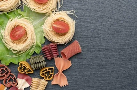 Pasta on the table, decorated with cherry tomatoes. Pasta of different shapes. Stock Photos