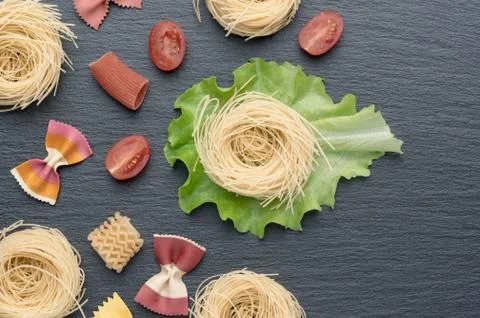 Pasta on the table, decorated with cherry tomatoes. Pasta of different shapes. Stock Photos