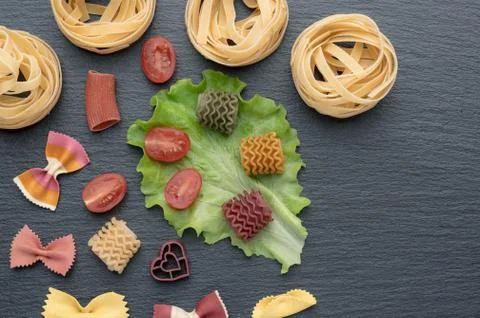 Pasta on the table, decorated with cherry tomatoes. Pasta of different shapes. Stock Photos