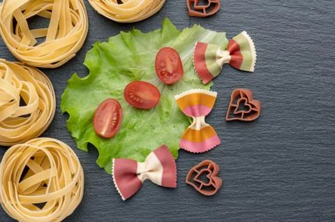 Pasta on the table, decorated with cherry tomatoes. Pasta of different shapes. Stock Photos