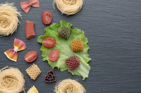 Pasta on the table, decorated with cherry tomatoes. Pasta of different shapes. Stock Photos