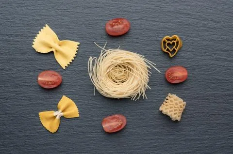 Pasta on the table, decorated with cherry tomatoes. Pasta of different shapes. Stock Photos