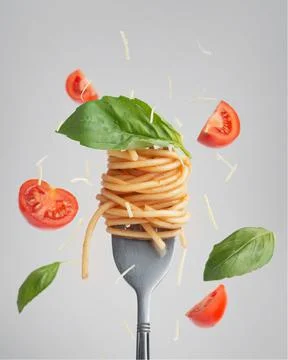Pasta with tomatoes and basil on a fork with levitating tomatoes and basil Stock Photos
