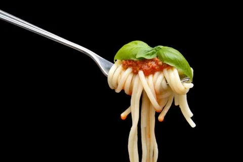 Pasta wound on fork with basil leaf on black background Stock Photos