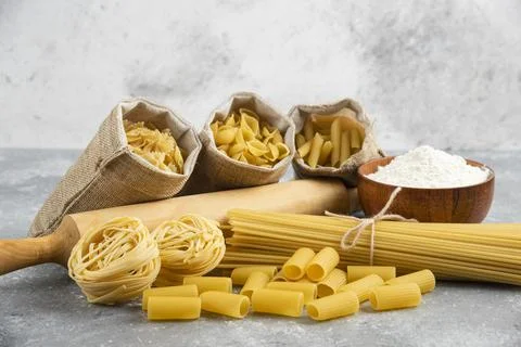 Pastas in rustic basket with rolling pin and a wooden cup of flour around Stock Photos