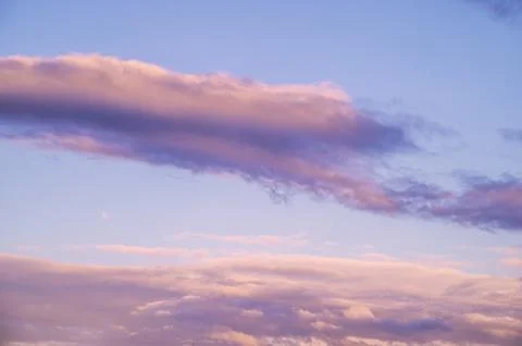 Pastel colored clouds drift across a serene blue sky at dusk Stockfoto's