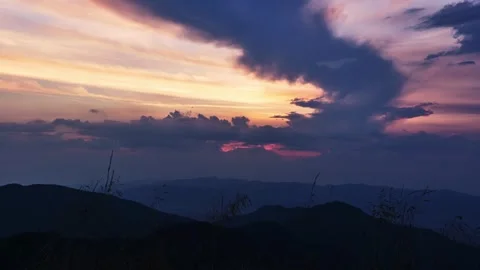 Pastel colored clouds form over the rolling hills of the landscape at sunset 스톡 동영상 285624207