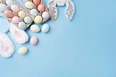 Pastel colored Easter eggs and bunny ears on blue background with copy space 库存照片