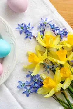 Pastel colored Easter eggs on a white plate and tablecloth, surrounded by b.. Stock Photos
