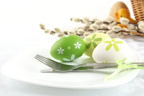 Pastel colorful three easter eggs on plate with cutlery and cart with duck in Stock Photos