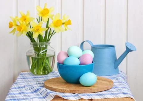Pastel dyed Easter eggs in a blue bowl with vibrant yellow daffodils in a g.. Stock Photos
