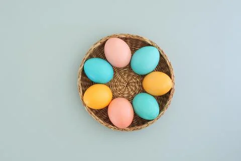 Pastel easter eggs in a basket on a blue background, top view, flat lay Stock Photos