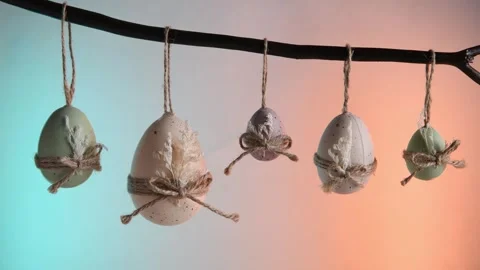 Pastel easter eggs in green, white, and purple hang from a natural branch, tied Stock Footage 332045016