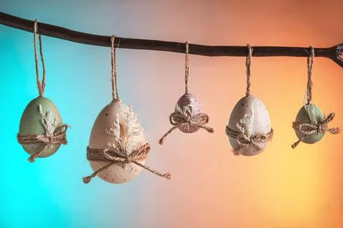 Pastel easter eggs in green, white, and purple hang from a natural branch, ti Stock Photos