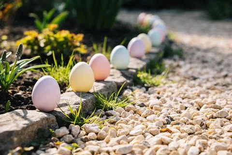 Pastel Easter eggs lined up in a garden path with sunlight and greenery Stock Photos